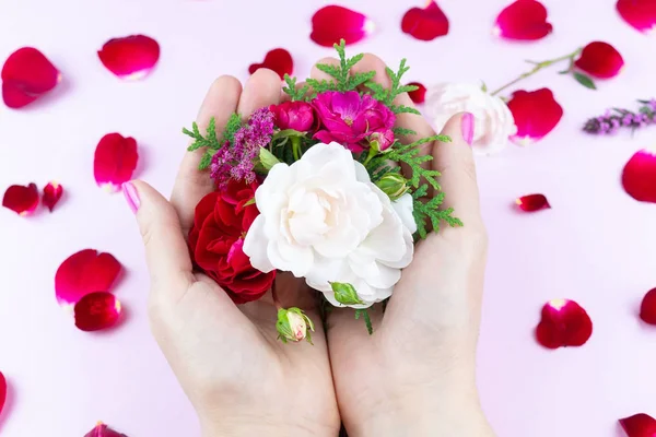 Beauty gentle hands with flowers and flower petals on pink background, hands with beautiful bright makeup and rose petals
