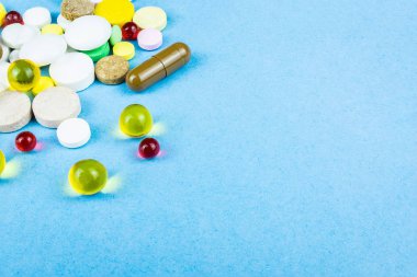 Çeşitli ilaç hapları, haplar ve kapsüller mavi arka planda.