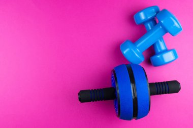 Spor malzemeleri: dambıllar, pembe arka planda basın için silindirler, fotoğraf afişi, üst görünüm, metin için boşluk.