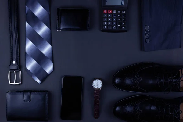 Business flat lay background with a copy space. Male shoes, wrist watch wallet,  belt, mobile phone and a necktie on black  background.