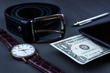 Erkek modası ve aksesuarları, siyah deri kayışlı bilek saati tükenmez kalem ve cüzdanımda bir dolar siyah arka plan.