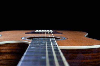 yellow guitar pick tucked into gold acoustic guitar strings on a dark wood fret board.	