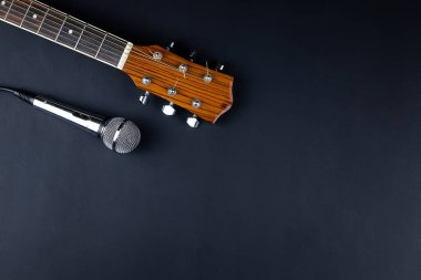 Klasik altı telli gitar boynu ve siyah arka planda gümüş bir mikrofon. Gitar ve aksesuarlar. Yaratıcılık ve gitar çalmak