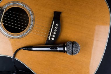 Klasik altı telli gitar boynu ve siyah arka planda gümüş bir mikrofon. Gitar ve aksesuarlar. Yaratıcılık ve gitar çalmak