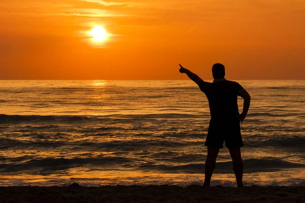 若い男が海で夜明けの太陽のことを指すのシルエット — ストック写真
