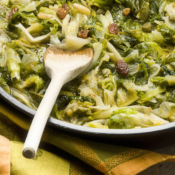 Closeup of Cooked Broad-leaved Endive Salad with pine nuts capers and raisin in Pan on a rustic wooden table