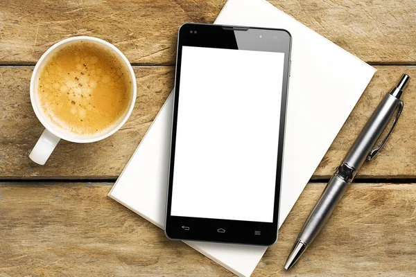 Top view of smartphone with blank screen on notepad next to a cup of coffee and ballpoint on a rustic wooden table