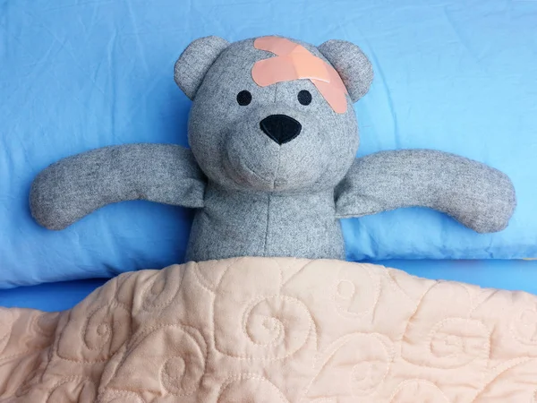 Injured Teddy Bear with plasters on head resting in the bed