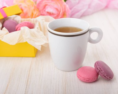 Ahşap bir tabloda çay fincan. Fransızca macaroons kutusunda. Kekler ve taze pembe çiçekler