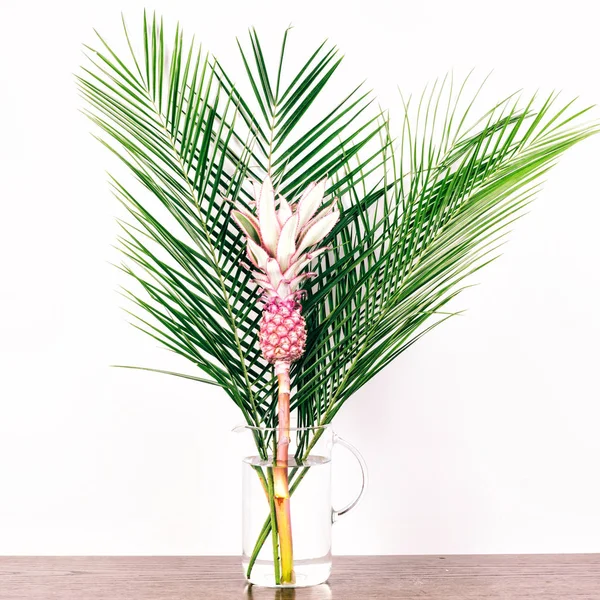 Tropical bouquet on a wooden table. Decorative pink pineapple and a palm branches in a vase. Summer vocation concept