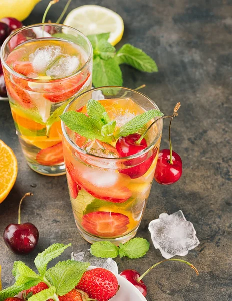 The glasses of lemon water. Lemonade with strawberry, mint and ice on a table. Sunny summer day