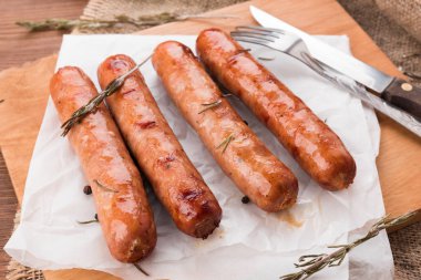 Karanlık bir rustik ahşap arka plan üzerinde ızgara sosis. Et sosis pişirme bir kağıt üzerine baharat ile