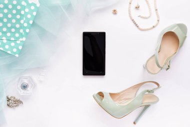 Kadının aksesuarları ve beyaz masa, üstten görünüm, smartphone lay düz. Turkuaz Ayakkabı ve tam balerin etek, inci kolye, parfüm şişe ile kadın çalışma alanı. Metniniz için kopya alanı