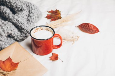 Kırmızı fincan kahve bir yatakta. Sıcak içecek sayfasındaki sıcak rahat gri ekoseli, sonbahar yaprakları ördü. Kraft zarf whith davet. Üstten görünüm veya düz lay, metniniz için kopya alanı