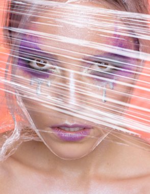 Kadın gümüş gözyaşları ile yaratıcı mor makyaj ile güzellik portresi plastik görünüyor. Güzel esmer selofan sarılı. Cadılar Bayramı kavramı