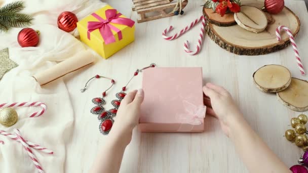 女性の手は ギフトのジュエリーのネックレスをラップし ボックスに置きます クリスマスと新年の祝日のための準備のプレゼント — ストック動画