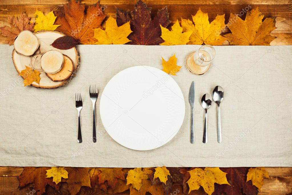 Top view of beautiful autumn decor and cutlery on wood table served for thanksgiving dinner. Fall maple yellow and red leaves