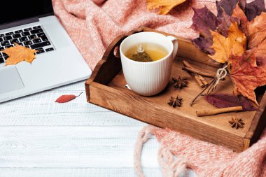 Ev ofis masaüstü ile bir dizüstü bilgisayar, sıcak sıcak pembe kareli, fincan çay tepsisi ve sonbaharda akçaağaç sarı ve kırmızı üzerinde bırakır. Ahşap beyaz masa, düz yatıyordu. Kış ve sonbahar arka plan, üstten görünüm