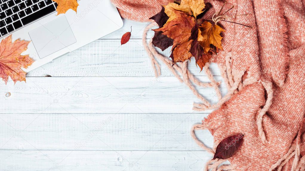 Home office desktop with a laptop, cozy warm pink plaid and autumn maple yellow and red leaves. Wooden white table, flat lay. Winter or autumn background, top view