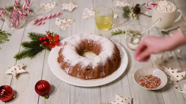 传统的圣诞水果蛋糕放在一张白色的木桌上 女性的手洒颜色甜美的顶部 Ttree 糖果棒 — 图库视频影像