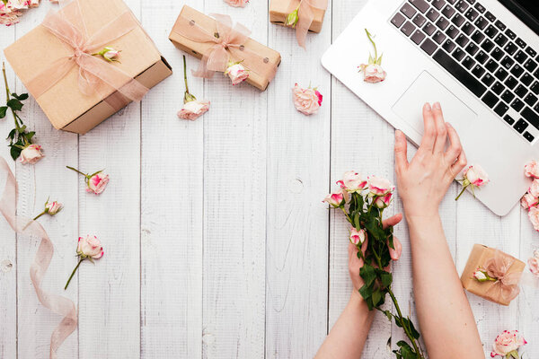 Рабочее пространство с клавиатурой ноутбука, розовые цветы, подарочные коробки
