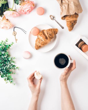 Beyaz masa üzerinde kahve, kruvasan, badem kurabiyesi ve çiçekler var.