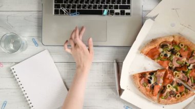 İş kadını bir dizüstü bilgisayar ile bir ofis masasında çalışan ve lezzetli bir pizza ve su bardağı ile bir öğle yemeği molası yaşıyor. Üst görünüm, düz yatıyordu