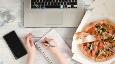 İş kadını bir dizüstü bilgisayar ile bir ofis masasında çalışan ve lezzetli bir pizza ve su bardağı ile bir öğle yemeği molası yaşıyor. Üst görünüm, düz yatıyordu