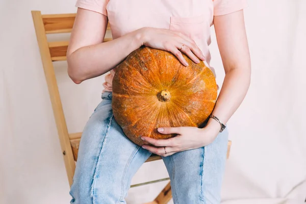 Mujer en jeans azules y camiseta rosa sosteniendo una calabaza grande — Foto de Stock