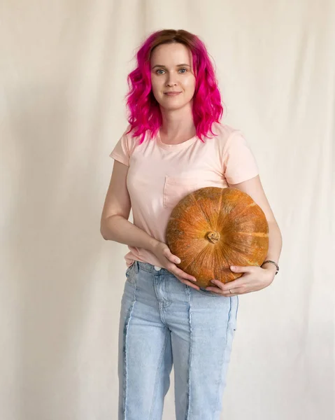 Mujer en jeans azules y camiseta rosa sosteniendo una calabaza grande — Foto de Stock