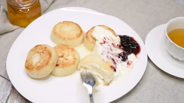 木製のテーブルの上にジャムとサワークリームとチーズパンケーキを食べる女の子 紅茶と甘いカッテージチーズデザート — ストック動画