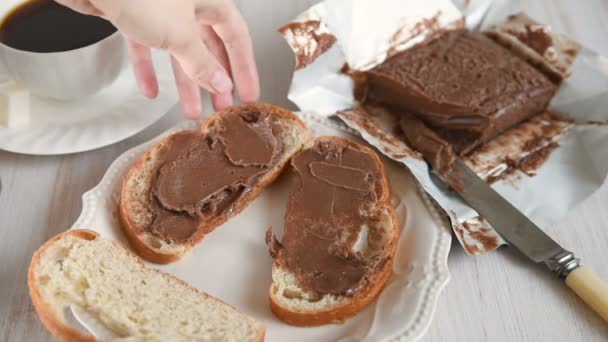 女性の手はパンのスライスにチョコレートバターを広げます コーヒーカップ 朝食コンセプト — ストック動画
