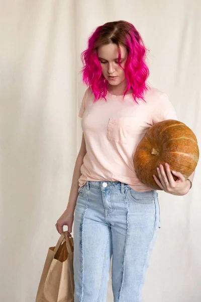 Mujer en jeans azules y camiseta rosa sosteniendo una calabaza grande —  Fotos de Stock