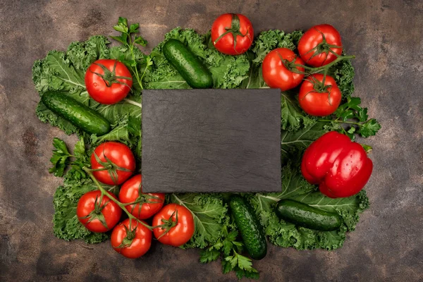 Kale salad leaf and red tomatoes, pepper, cucumbers, avocado with water drops on an old rustic metal tray. Green nature background. Black stone chalk board for copy space