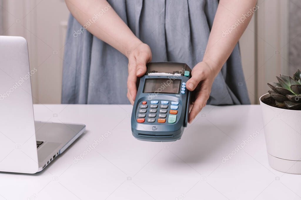 Female hands holding NFC payment terminal in a shop. Credit card or phone pay pos banking device, card machine on a white table.