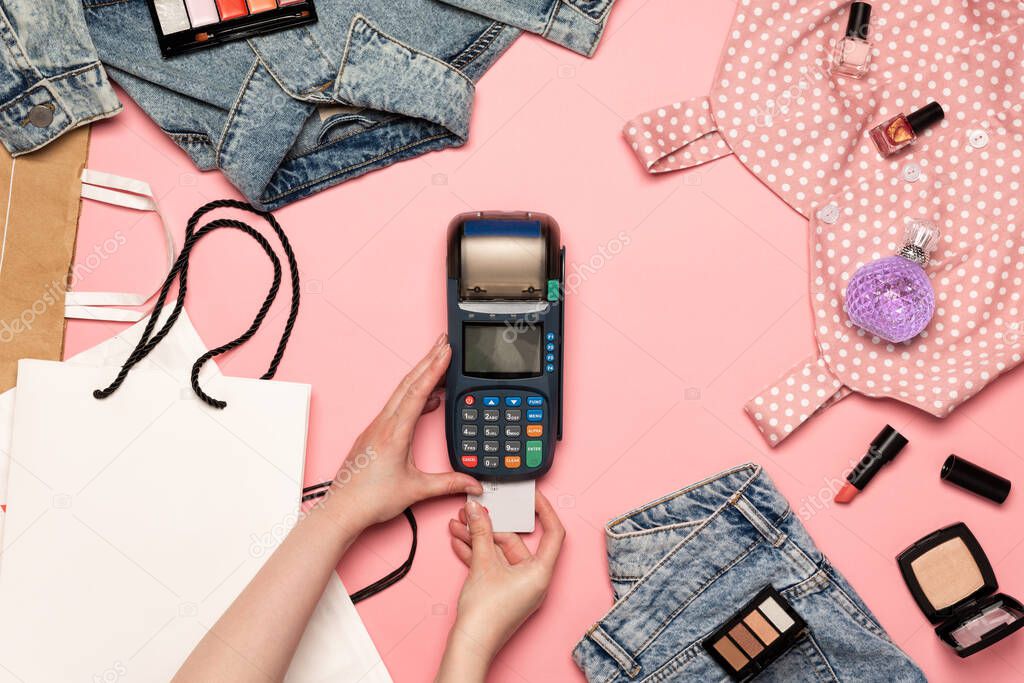 Woman paying by card on NFC payment contactless terminal on a pink background. Credit card or phone pay pos banking device. Female shopping, flat lay