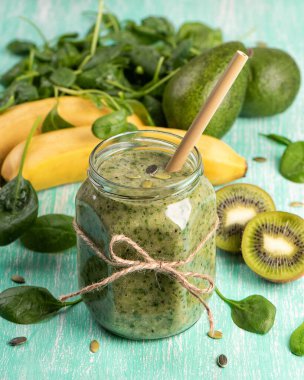 Cam bir kavanozda yeşil detoks smoothie muz, kivi, turkuaz arka planda ıspanak. Vitaminli sağlıklı içecek.