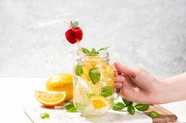 Bir bardak limonata ya da limonlu, portakallı ve fesleğenli mojito kokteyli. Mermer kesme tahtasındaki buzlu soğuk içecek ya da içecek.