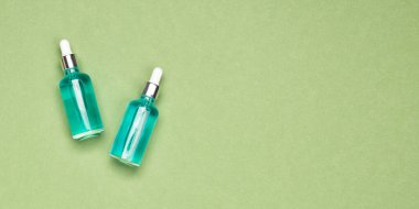 Yeşil arka planda damlatan cam şişedeki nemlendirici güzellik özü ya da serum. Spa kozmetik konsepti, metin için kopyalama alanı olan pankart
