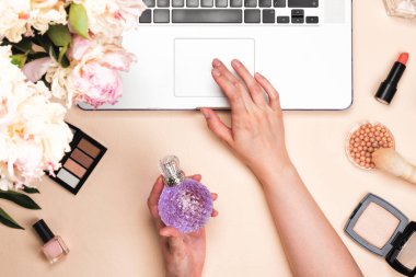 Dizüstü bilgisayarı, kozmetik ürünleri ve pastel pembe masasında şakayık çiçekleri olan bir blog yazarı çalışma alanı. Düz yatış, üst görünüm