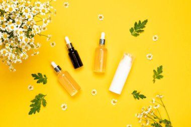 Cam esans şişeleri ya da papatya çiçekli serum. Sarı arka planda nemlendirici yüz kremi ve papatya.