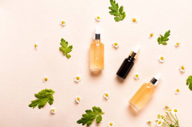 Cam esans şişeleri ya da papatya çiçekli serum. Pembe arka planda nemlendirici yüz kremi ve papatya.