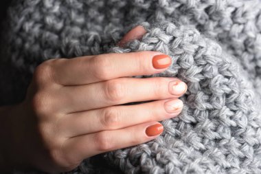 Turuncu renkli sonbahar mermer manikürlü kadın elleri. Gri örülmüş yün kazak ya da ekose