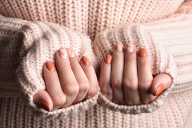 Turuncu renkli sonbahar mermer manikürlü kadın elleri. Pembe örülmüş yün kazak.