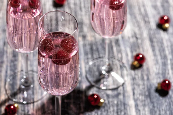 Pink sparkling cocktail with a raspberry. Glass of champagne and Christmas bubbles on wooden table with on wooden table