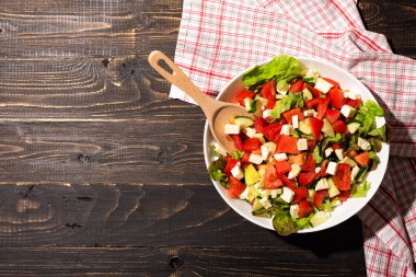 Taze marul, domates, salatalık ve peynirli organik sebze salatası. Tahta masada bir kase sağlıklı diyet yemeği. Üst görünüm, alanı kopyala