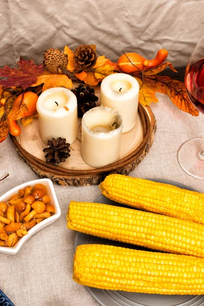 fall decoration and candles on festive autumn holiday table setting with corn, peas, pickled mushrooms. Thanksgiving family dinner. Maple leaves