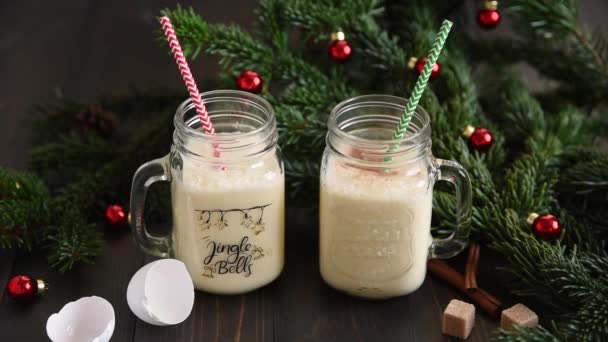 伝統的なクリスマスは カクテルシェーカーからガラスマグカップに卵を飲みます シナモン暗い木製のテーブルの上に星をアニスします 飴杖とモミの木の装飾 — ストック動画