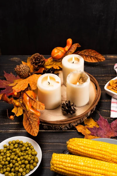 fall decoration and candles on festive autumn holiday table setting with corn, peas, pickled mushrooms. Thanksgiving family dinner. Maple leaves