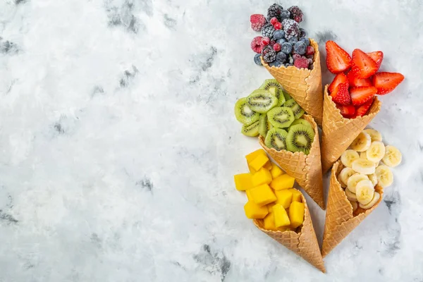 Concepto de dieta saludable - frutas y bayas congeladas en conos de helado sobre fondo rústico —  Fotos de Stock